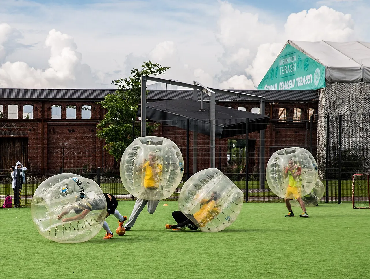 Partie de bubble foot en extérieur, un joueur renversé dans sa bulle près du ballon